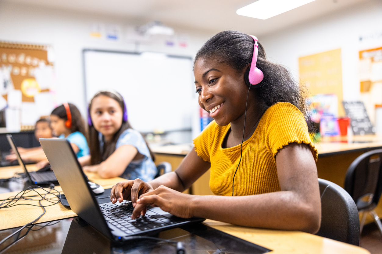 Students learning on laptops with headphones in a bright classroom